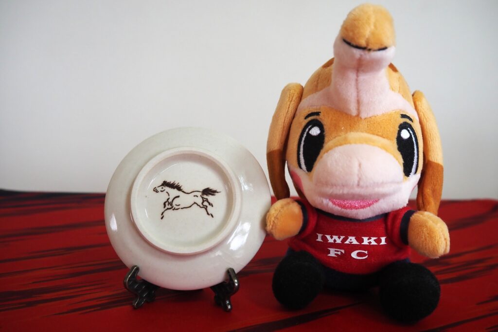 The "Hashirikoma" on the back of the small plate and "Hamadori," the Iwaki FC mascot.